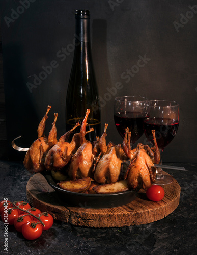 Roasted stuffed quail on a spit and red wine on a dark table. photo