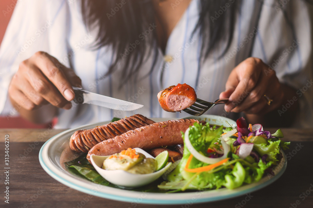 A woman eating grilled sausage, in morning.