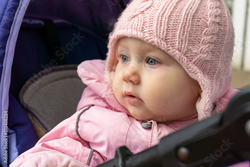 A little girl in a pink jacket in a pram looks around.