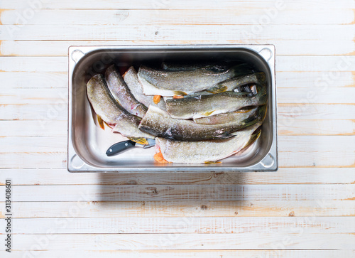 crude fresh pike in metal container on wooden photo