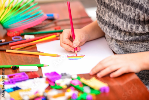 A girl draws a heart with colored pencils on a white sheet among children's toys.