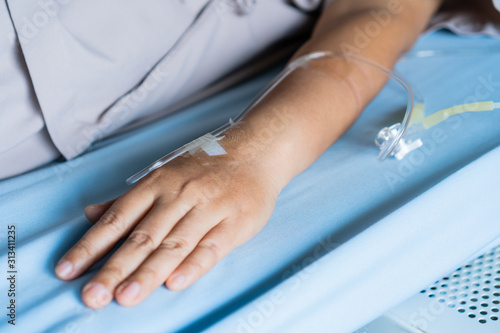 Patients saline  Iv drip  young woman hand with medical drip intravenous needle  give salt water on hospital bed. intravenous therapy  IV  is a therapy that delivers fluids directly into vein.