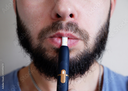 Bearded man smokes an electronic cigarette close-up. New technology for healthy smoking electronic cigarettes vaping. IQOS concept.