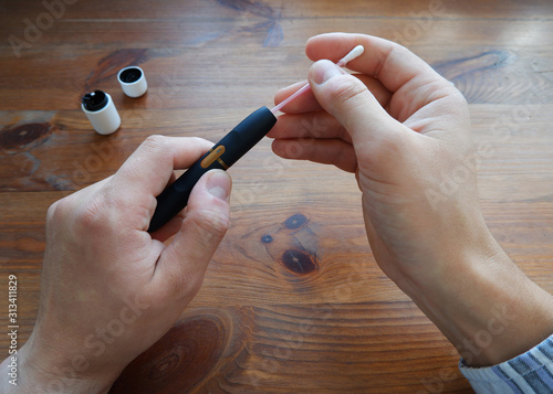Принти на полотні A man in a plaid shirt cleans an iqos electronic cigarette