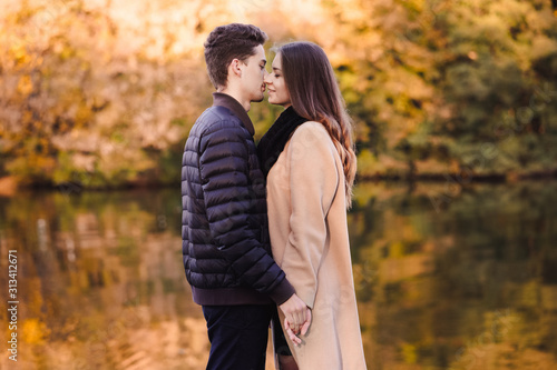 Couple in love standing in autumn park with yellow fallen leaves. Man and woman enjoying a day together. Boy kissing a girl in lips