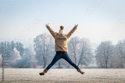 Happy woman jumping with arms outstretched in winter nature