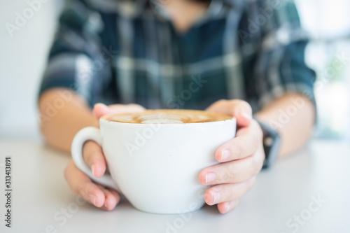 Woman hand holding a white coffee mug.  Coffee is a latte. table on the wooden table in vintage style  taken from the top view  see the froth of milk foam.