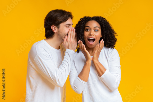 Young man sharing secret with his shocked black girlfriend