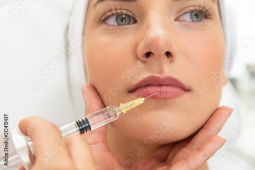 Powiększenie ust kwasem hialuronowym. Zbliżenie na usta kobiety podczas zabiegu modelowania ust. Kosmetolog wstrzykuje wypełniacz, medycyna estetyczna.  photo