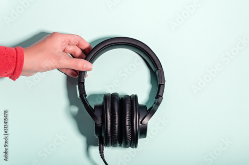 Black massive headphones in female hand on pastel background, copy space. Modern technology flat lay with over-ear earphones in woman hand, modern lifestyle concept