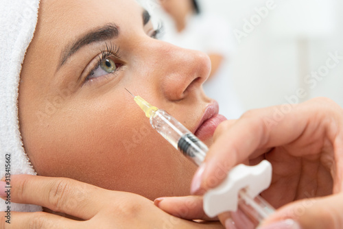 Kosmetolog wykonuje zabieg przeciwzmarszczkowy. Ostrzykiwanie toksyną botulinową, redukcja zmarszczek. Botoks w klinice medycyny estetycznej. Wstrzykiwanie wypełniacza pod oczy. 