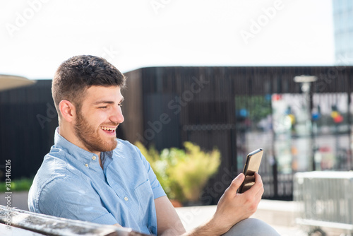 Side of happy young man sitting outside looking at cellphone