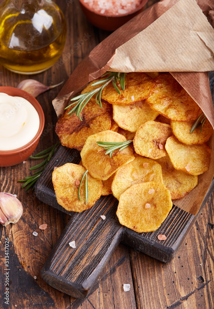 Fototapeta premium Crispy potato chips. Slices of potato, roasted with sea salt and rosemary. Delicious snack served with sauce. Fast food.