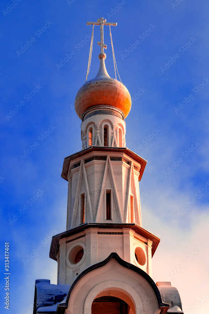 Bell tower of Orthodox Church in Russia against blue sky.