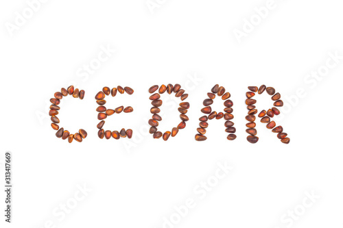 Word "CEDAR" spelled with pine nuts isolated on white background. Food pattern made from nuts. Flat lay, copy space for text