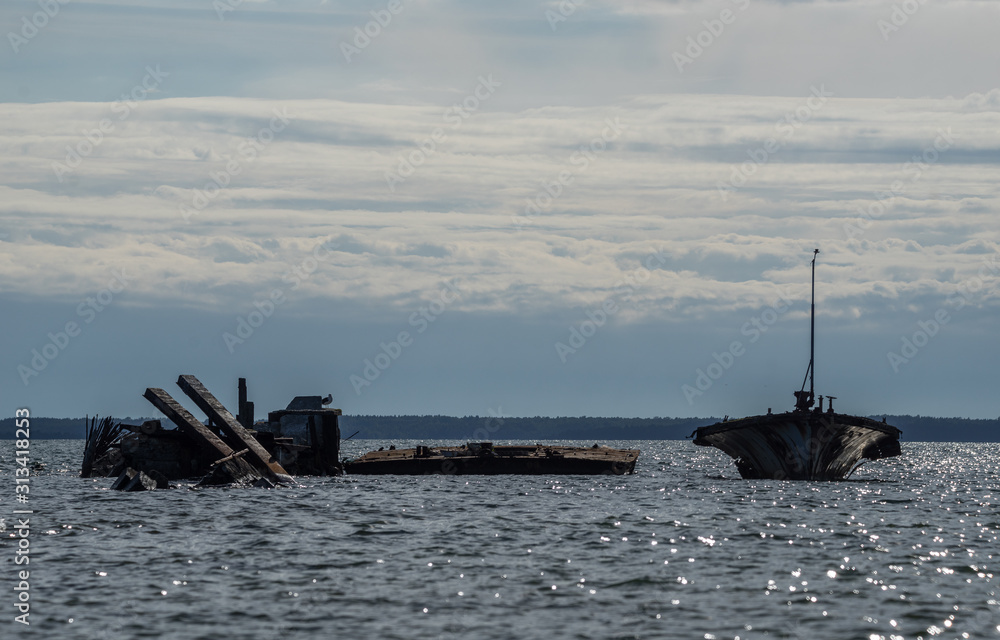 Old broken boat wreck on the shore, blue sea and sailboat on background. Harilaid, small island in Estonia, Europe.