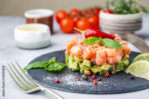 Delicious avocado and raw salmon salad, tartare, served on a black plate with lime, light background