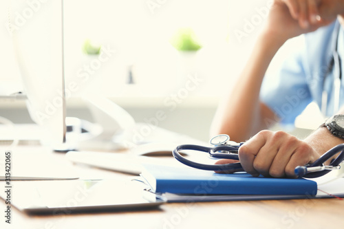 Serious male doctor looking at computer monitor while holding stethoscope in one hand and propped his head with other hand.