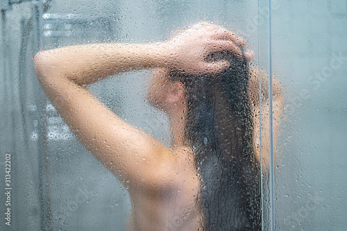 Foto Unfocused naked woman showering, bathing and washing long hair in shower under r