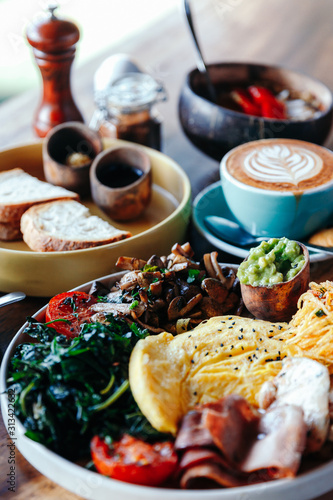 Morning breakfast on a table, waffles with cream, berries, coffee, cappuccino, bowl, omlet with vegetables, bread with butter, avocado cream, vegan food, healthy food, meal.