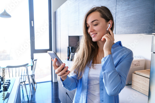 Foto Attractive happy mobile modern woman uses wireless white headphones and smartpho