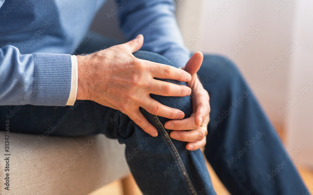 Senior man massaging his knee sitting on sofa indoor, cropped Senior man massaging his knee sitting on sofa indoor, cropped