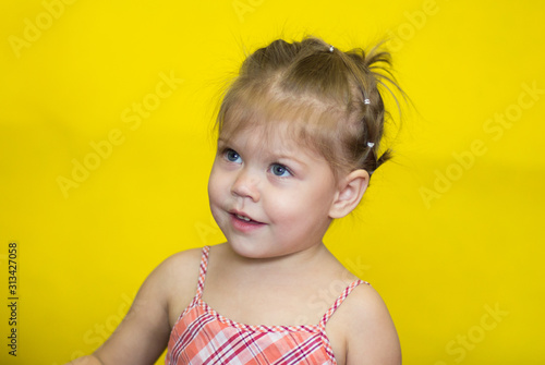 Portrait of caucasian little girl with playful look of two year old on the yellow background looking aside