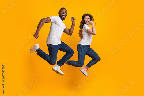 Funny interracial couple jumping and running in the air, yellow background