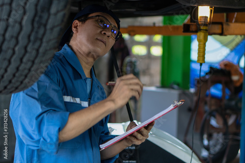 portrait of asian male car mechanic performing car checking and maintenace service at garage and car maintenance service station