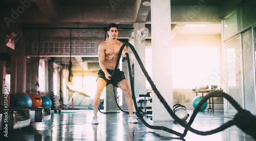 Sports man with battle rope battle ropes exercise in the fitness gym. Fitness, gym, sport, rope, training, athlete, workout, exercises and healthy concept