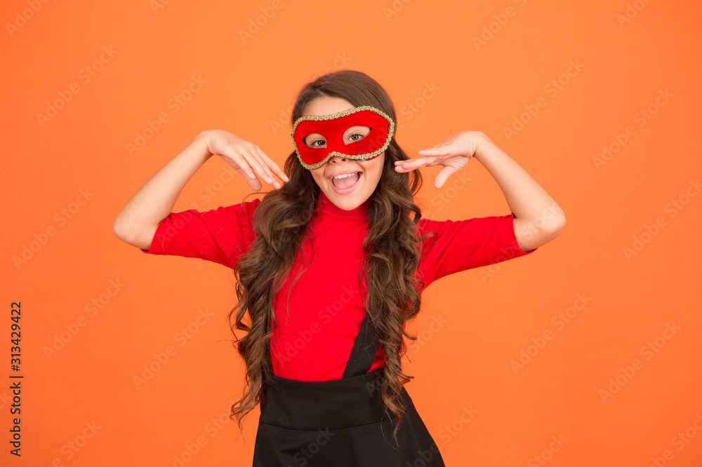 Change your look. Happy child with party look orange background. Vogue look of small fashion model. Little girl wear carnival mask. Beauty look. Festive fashion accessory. Holiday celebration Change your look. Happy child with party look orange background. Vogue look of small fashion model. Little girl wear carnival mask. Beauty look. Festive fashion accessory. Holiday celebration