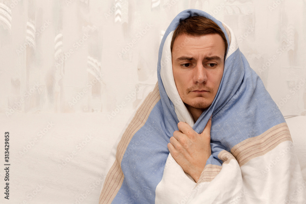Colds and flu. The guy wrapped in a blanket sits on the bed