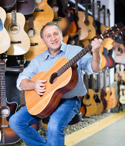 Adult guitarist is playing on acoustic guitar in music store.