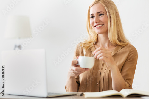 Happy entrepreneur woman drinking coffee  working on laptop