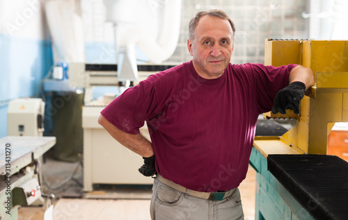 Portrait of elderly foreman in protective gloves standing in workshop
