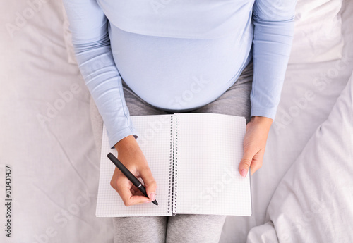 Unrecognizable Pregnant Woman Taking Notes Sitting On Bed Indoor, Top-View