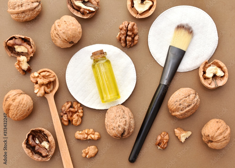 Walnut oil in small bottle, cosmetic brush, natural skin and hair care product, flat lay on brown background. 