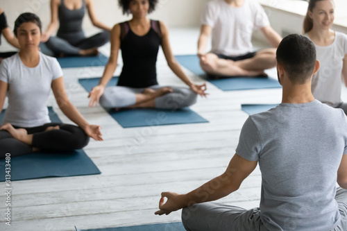 Trainer teaching diverse people practicing yoga, doing Padmasana exercise