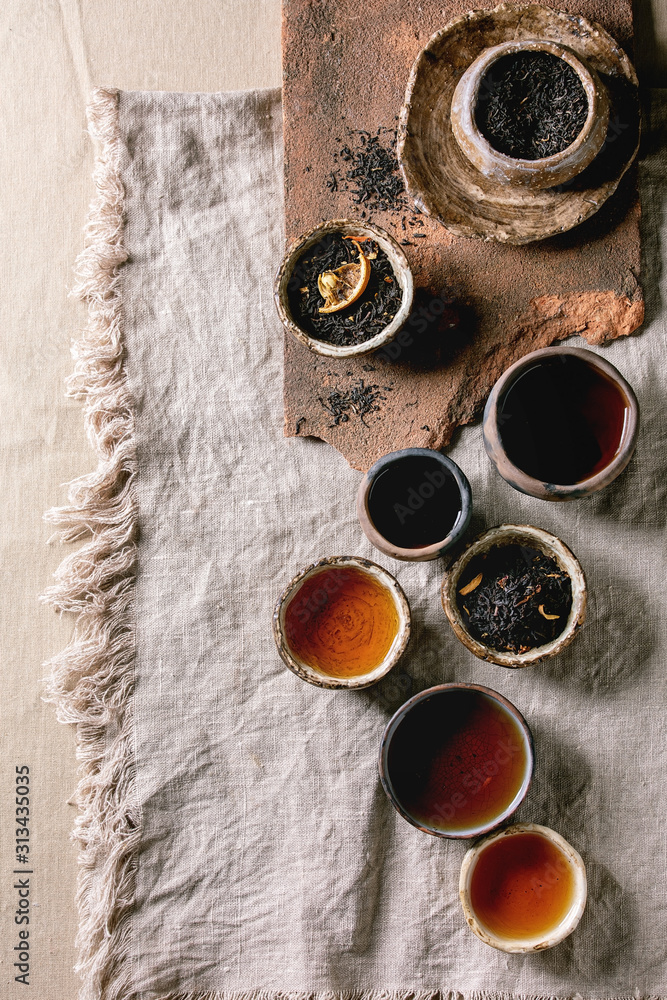 Variety of hot and dry tea green and black in traditional and wabi sabi style fireclay ceramic craft cups and bowls, served on linen cloth as background. Flat lay, space