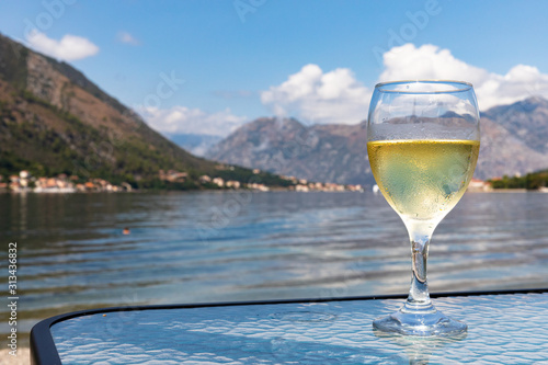 glass of white wine on glass table in front of lake in kotor