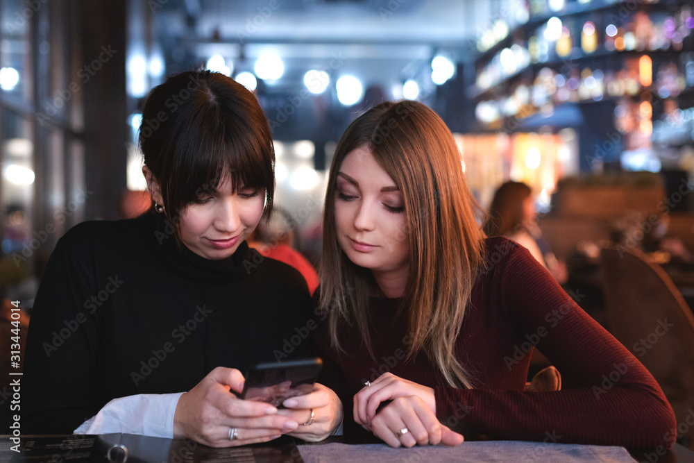 Young pretty women sitting in restaurant and watching at smartphone. Making online order at bar market.