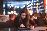 Beautiful young caucasian woman sitting in restaurant and looking at menu choosing what to order. Dinner outdoor. Visiting cafe in evening after job. reading menu.