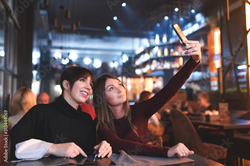 Smiling and happy Girlfriends making selfie at the restaurant table at the dinner with a smartphone.