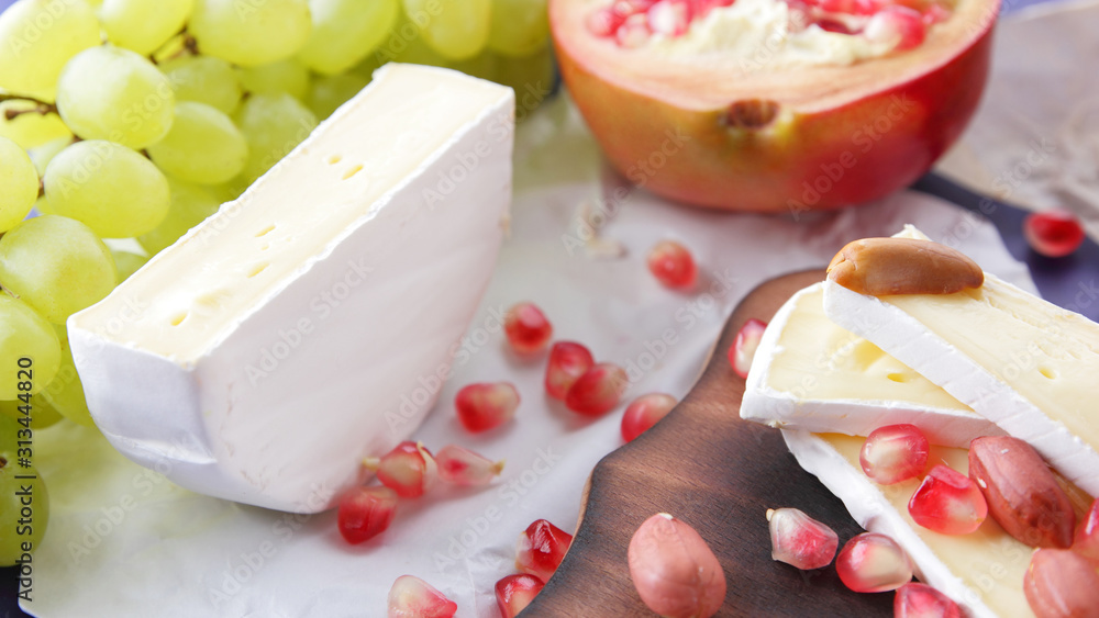 Cheese platter: variety of cheeses on wooden plate with fruits and nuts. Different types of cheese. Camembert, grapes and pomegranate on a classic blue background Cheese platter: variety of cheeses on wooden plate with fruits and nuts. Different types of cheese. Camembert, grapes and pomegranate on a classic blue background