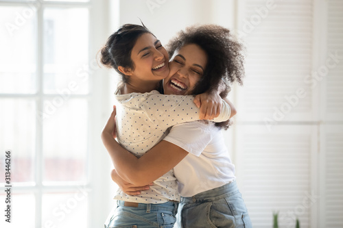 Fotografie Happy multiethnic girlfriends have fun hugging indoors