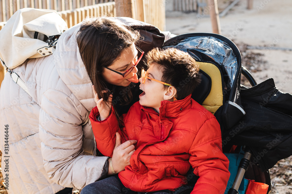una madre juega con su hijo con pluridiscapacidad en un parque, el niño ...