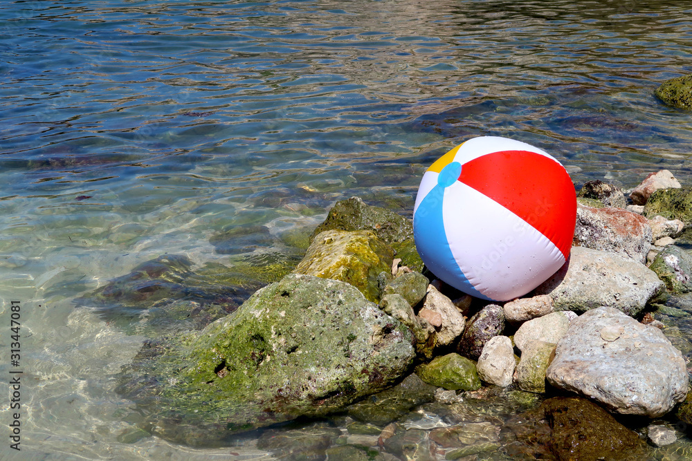 Inflatable beach ball on the rock beach in Italy with sea in the background - summer holiday vacations concept - Italy, Monopoli, Adriatic Sea