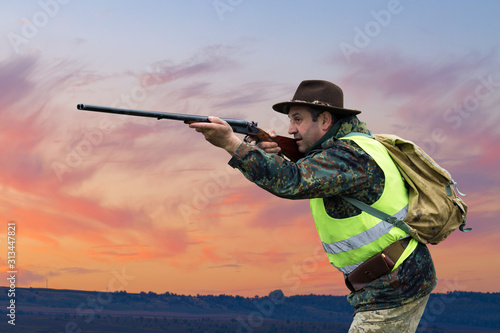 Silhouette of a hunter on the background of the morning red dawn. Stands at the ready with a gun.