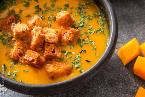 Vegan pumpkin soup in black ceramic bowl on dark background, top view