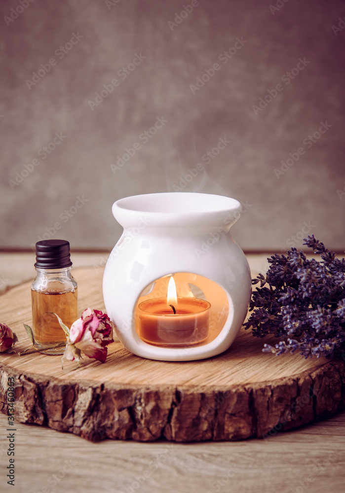 Vintage style picture of white ceramic candle aroma oil lamp with essential  oil bottle and dry flower petals on natural pine wood disc, dry background  with copy space. foto de Stock